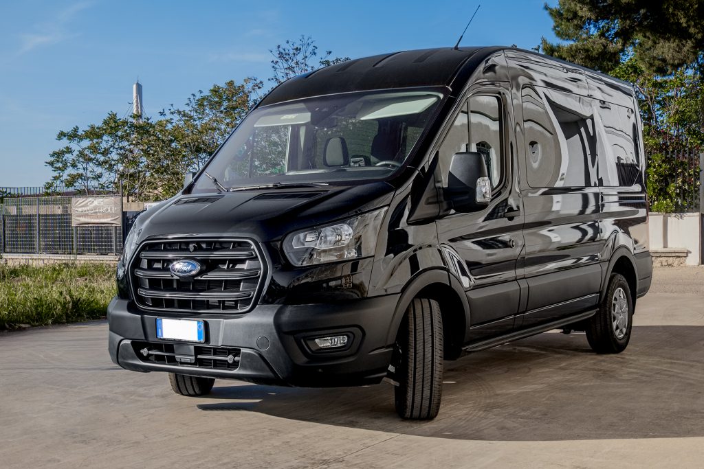 Ford Transit nero lucido della flotta Gioand Group parcheggiato su piazzale in cemento, alberi e cielo azzurro sullo sfondo