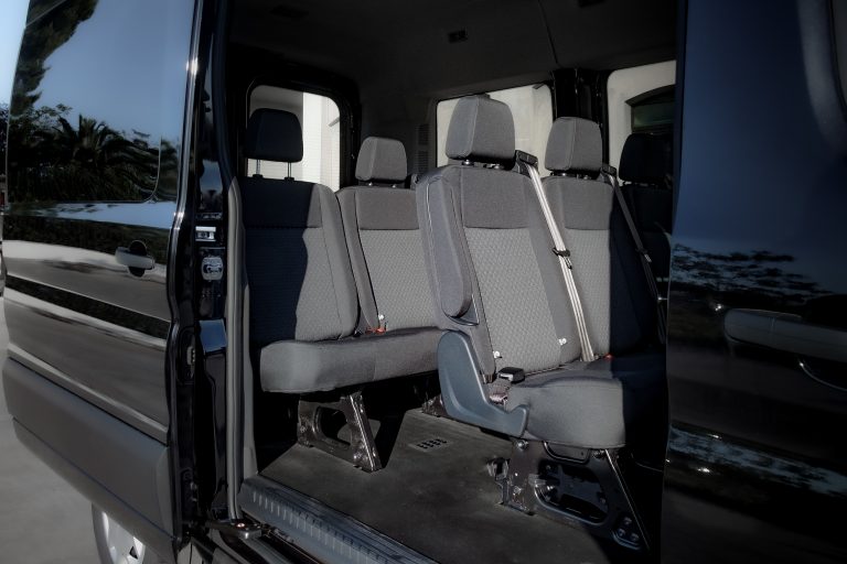 Interno di minivan nero con portellone laterale aperto, sedili in tessuto grigio con cinture e pianale scuro