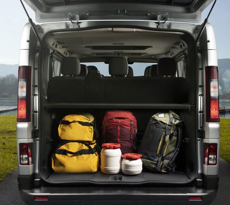 Bagagliaio aperto di un minivan grigio con borsoni gialli, zaini rosso e verde e bidoni bianchi sotto i sedili posteriori